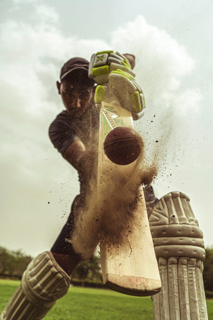 A cricket batsman hitting a ball with a wooden bat on a field