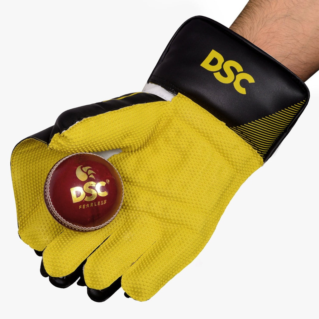 DSC Condor Ruffle adult wicketkeeping glove holding a red cricket ball against its yellow grip palm
