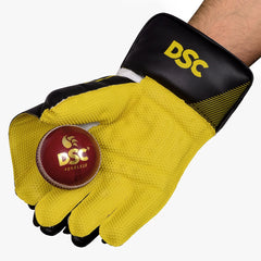 DSC Condor Ruffle adult wicketkeeping glove holding a red cricket ball against its yellow grip palm